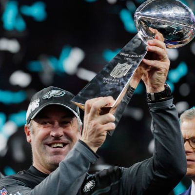 Alison Harbaugh's father, John William Harbaugh posing for a photo shoot while holding the trophy in both hands. 